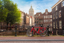 Houses And Boats On Amsterdam Canal. Morning Photo Of Colored Houses In The Dutch Style And Bridge With A Red Bicycle In The Foreground