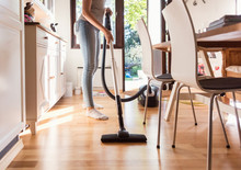 Low Section Of Teenage Girl Cleaning Hardwood Floor With Vacuum Cleaner At Home
