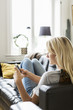 © Maskot - Teenage girl using phone while reclining on sofa at home