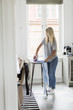 © Maskot - Teenage girl ironing clothes against window at home