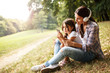 © BalanceFormCreative - Mother and daughter sitting on grass and listening to music on smart phone.
