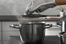 Woman Hand In Mitten Holding Lid Above Metal Pan In Kitchen