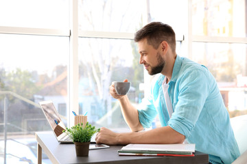 Sticker - Handsome young man drinking coffee while working with laptop at home