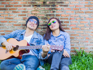 Poster - Hipster man playing guitar for his girlfriend outdoor against br