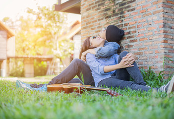 Poster - Hipster man playing guitar for his girlfriend outdoor against br