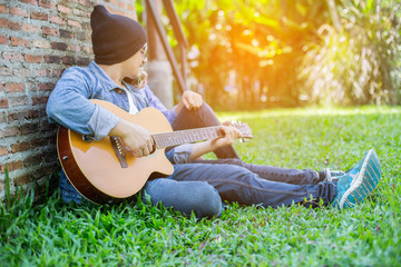 Wall Mural - Hipster man playing guitar for his girlfriend outdoor against br