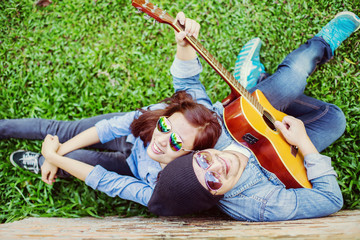 Wall Mural - Hipster man playing guitar for his girlfriend outdoor against br