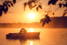 Love And Romantic Golden River Sunset. Silhouette Of Couple On Boat Backlit By Sunlight