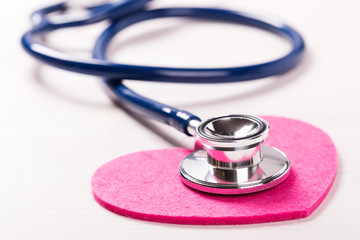 Stethoscope on heart shape over white wooden background