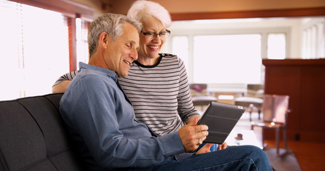 Senior couple sitting on couch watching videos on tablet