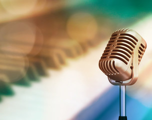 Vintage micro phone with blurred piano keyboard and bight light background, soft focus