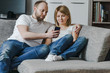 © Alexander - Natural, lifestyle image of attractive couple sitting on couch together looking at smartphone in the living room.