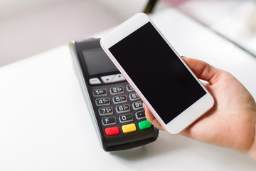 Woman hand with mobile phone using NFC (near field communication) technology for payment in the shop.