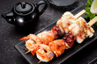 Tasty seafood skewers and soy sauce over dark concrete background