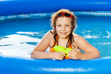 Wall Mural - Happy girl playing with water gun in the pool