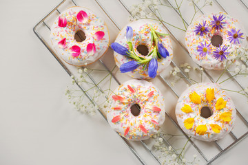 Poster - Delicious donuts and flowers on baking rack and light background