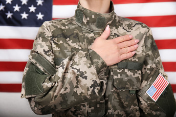 Wall Mural - Close up view of female soldier holding hand on heart, with USA flag on background