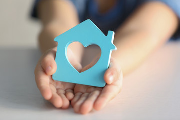 Child holding figure in shape of house, closeup. Adoption concept