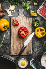 Wall Mural - Bell colorful paprika peppers cooking preparation. Paprika on wooden cutting board with kitchen knife, minced meat, egg and seasoning on dark rustic background, top view