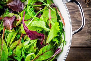 Wall Mural - Fresh salad with mixed greens on wooden background closeup