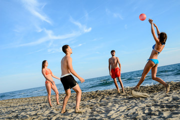 Wall Mural - four young people man and woman playing beach volley together by the sea in sunny summer vacation day