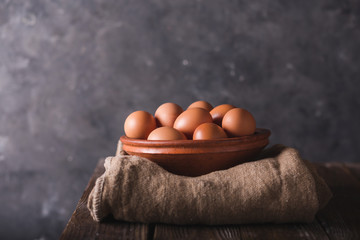 Brown eggs in a brown ceramic bowl on sacking and wooden table on an gray abstract bbackground. Rustic Style. Eggs.  Easter photo concept. Copyspace