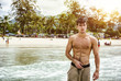 © theartofphoto - Heavily filtered shot of a handsome young man standing on a beach in Phuket Island, Thailand, shirtless wearing boxer shorts, showing muscular fit body