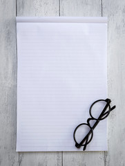 Wall Mural - Blank white note pad and eyeglasses on white wood background