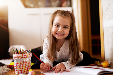 Cute little girl coloring drawings in a coloring book.