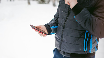  a young man with a beard, smokes an electronic cigarette and happily talking on the phone through the Internet, a positive relaxing outdoors in the snow in the winter