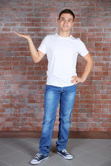 Wall Mural - Handsome young man in blank white t-shirt standing against brick wall