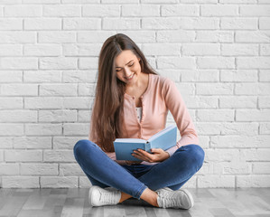 Poster - Beautiful young woman with book sitting on floor near brick wall