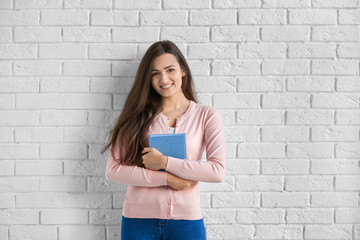 Canvas Print - Beautiful young woman with book standing near brick wall