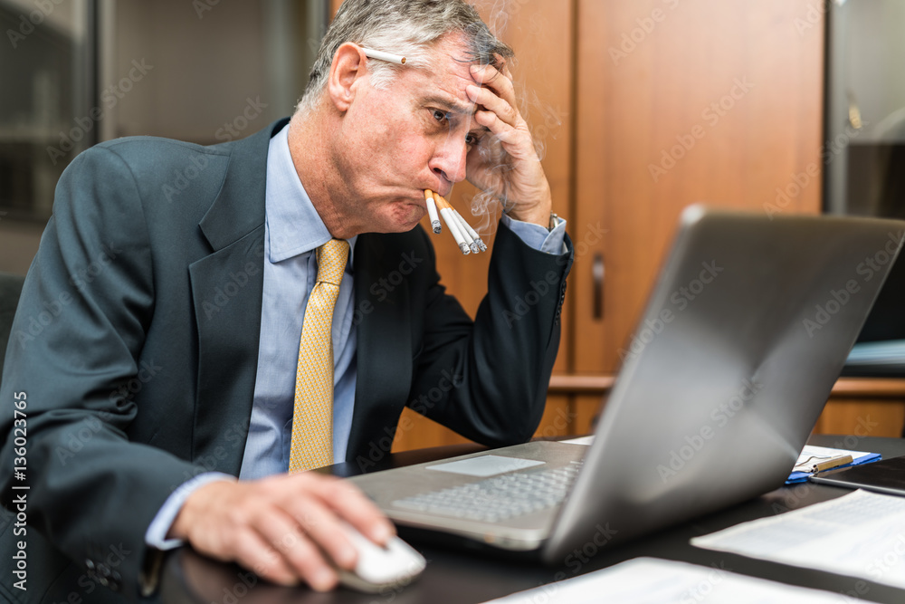 Nervous businessman smoking a lot of cigarettes at once while looking at  his computer Stock Photo