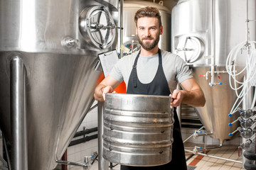 Wall Mural - Worker carrying barrel with beer at the brewery with metal containers on the background