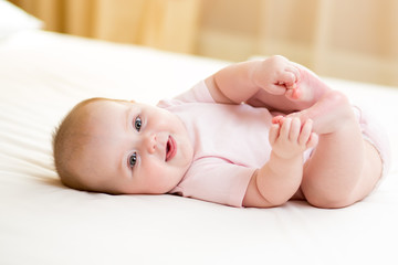 Wall Mural - happy baby girl lying on white sheet and holding her legs