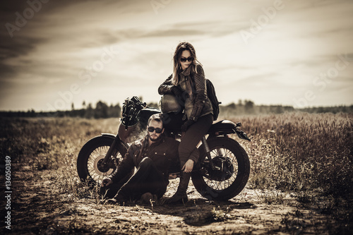 Fotomural Young, stylish cafe racer couple on vintage custom motorcycles in field