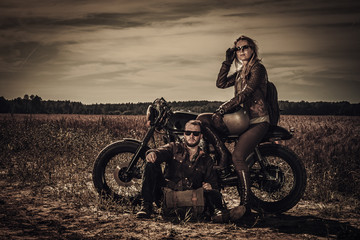 Young, stylish cafe racer couple on vintage custom motorcycles in field