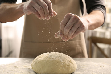 Poster - Man sprinkling flour over fresh dough on kitchen table