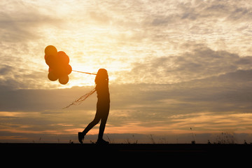 Silhouette of girl with balloons in the sunset background.