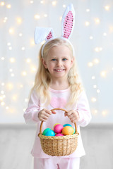 Wall Mural - Cute funny girl with bunny ears and basket full of Easter eggs at home