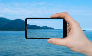 Wall Mural - A man  hand holding smart phone making photo on smartphone mobile closeup sea view