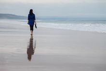 Young Woman Walking Alone In A Deserted Beach Reflected On The Wet Sand On An Autumn Day.