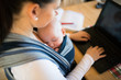 © Halfpoint - Unrecognizable mother with son in sling, writing on notebook