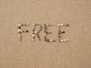 word free written with stones and shells on the beach by the ocean