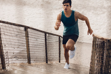 Fitness man running up the steps on beach