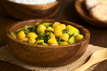 Wall Mural - Vegan chickpea curry or chana masala with spinach, potato and carrot served in wooden bowl, photographed with natural light (Selective Focus, Focus one third into the curry)