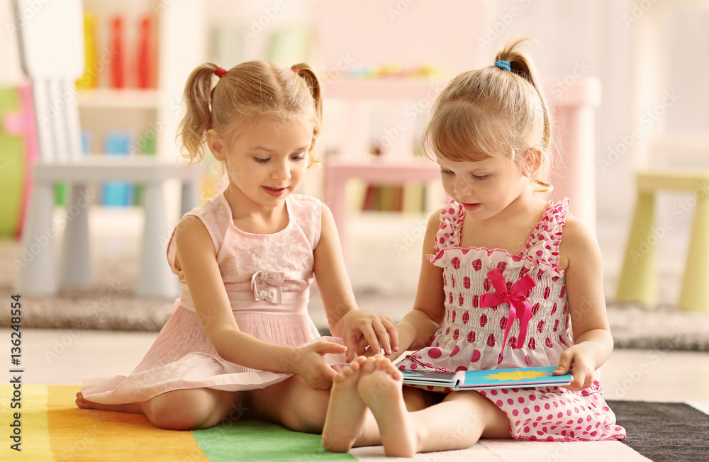 Cheerful little girls with book sitting on the floor Stock Photo ...