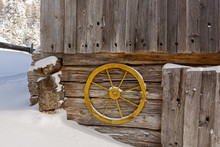 Old Yellow Wagon Wheel Hanging On Wall To Decorate Rustic Wooden Barn Wall With Cold Snow Winter Scene In Austria, Europe