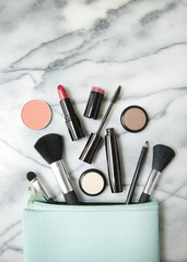 Wall Mural - Aerial view of make up products spilling out of a pastel blue cosmetics bag, on a white marble counter top background